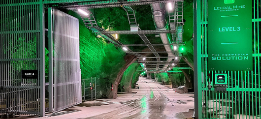 An open gate lit with green lights leading into an underground tunnel.