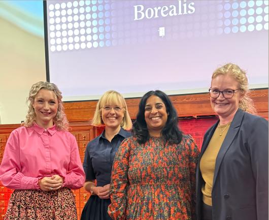 Four women smiling together on stage in front of a presentation screen reading "Borealis".