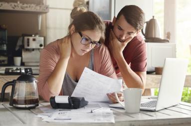 A young couple looking at bills in a kitchen setting. 