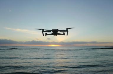 A flying drone over an ocean with a sunset in the background. 