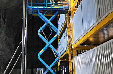An elevated lift in front of large containers. 